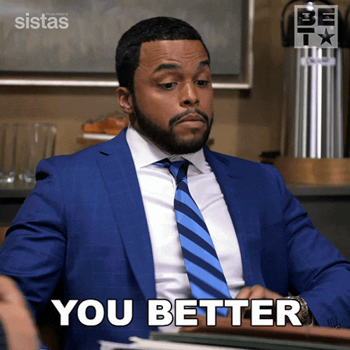 a man in a blue suit and tie is sitting at a desk and says you better