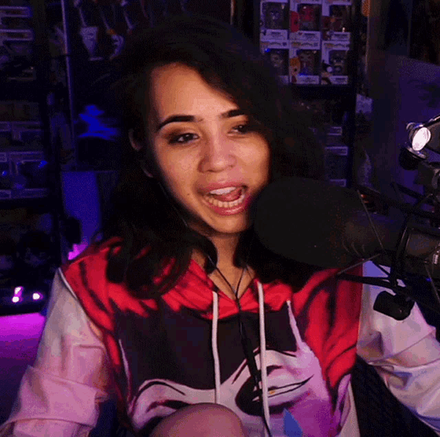 a woman wearing a red and black hoodie is smiling into a microphone