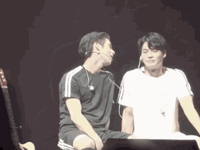 two men are sitting next to each other on a stage and one of them is wearing a microphone .