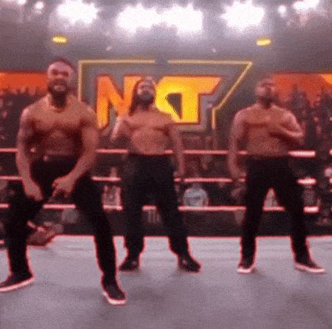 three men are dancing in a wrestling ring with the letters nt on the wall