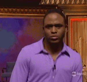 a man in a purple shirt is standing in front of an abc family sign .