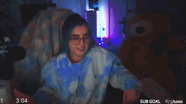 a girl with blue hair and glasses is sitting in front of a microphone with the time 3:04