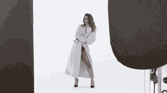 a woman in a white coat and black heels is standing in front of a white wall .