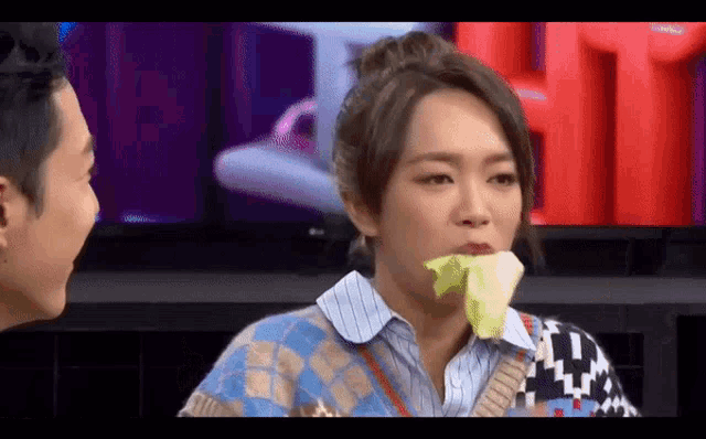 a woman is holding a piece of lettuce in her mouth while a man looks on .