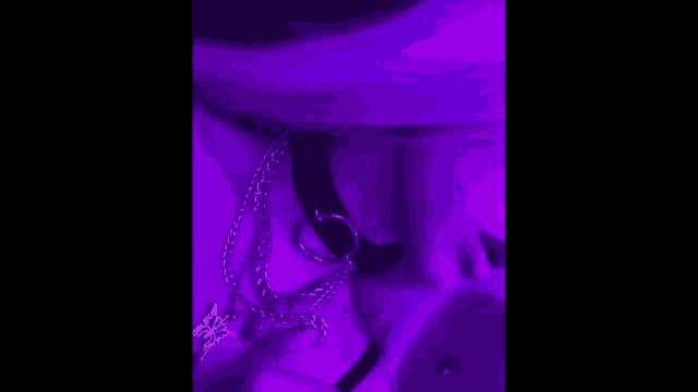 a woman wearing a choker and chains is standing in a purple light .