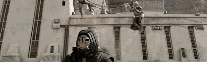 a man in a mask is standing in front of a building with a statue in the background .