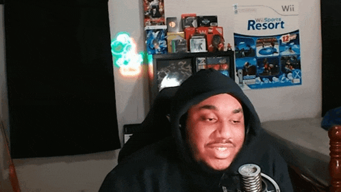 a man wearing a black hoodie is sitting in front of a wii poster