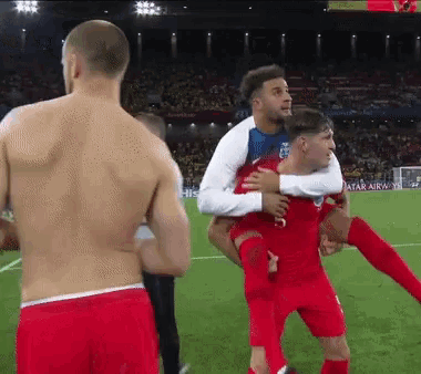 a shirtless soccer player is carrying another shirtless soccer player on his back on a field .