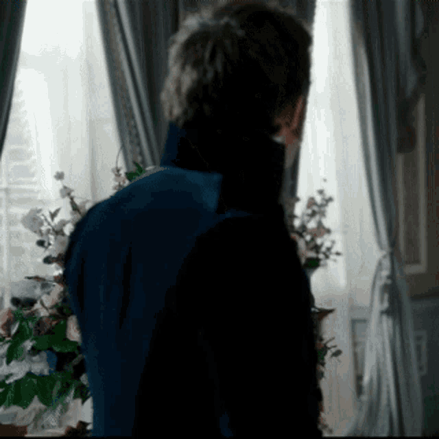 a man in a blue jacket is standing in front of a window