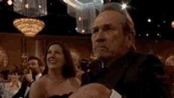 a man in a tuxedo and bow tie is sitting in a crowd of people .