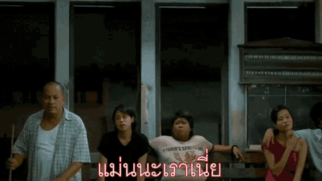 a group of people are sitting in a room with a sign that says ' แม่ นา ' on it