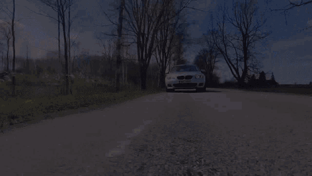 a white bmw is driving down a gravel road with trees in the background