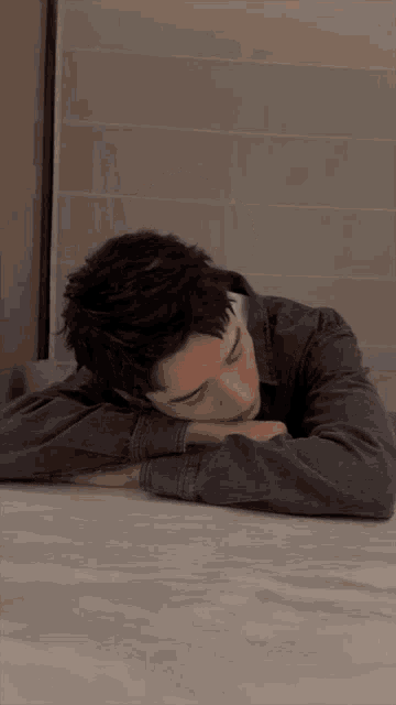 a young man is laying on a table with his head on his hands .