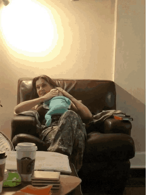 a woman sitting on a couch holding a baby and a starbucks coffee cup