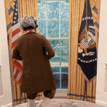 a man in a brown coat stands in front of a flag that says united states of america on it