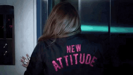 a woman wearing a black jacket with the words `` new attitude '' embroidered on the back .
