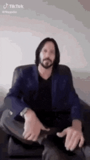 a man with a beard is sitting in a chair and making a funny face with his hands .