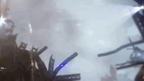 a crowd of people standing in front of a stage at a concert with smoke coming out of it .