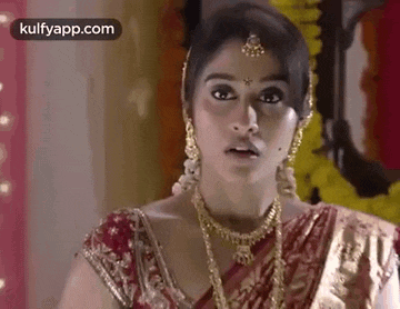 a close up of a woman wearing a red and gold sari and jewelry .