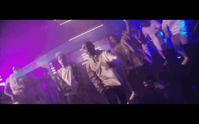 a group of young people are dancing in a dark room with purple lights .