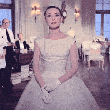 a woman in a white dress and white gloves is standing in a room