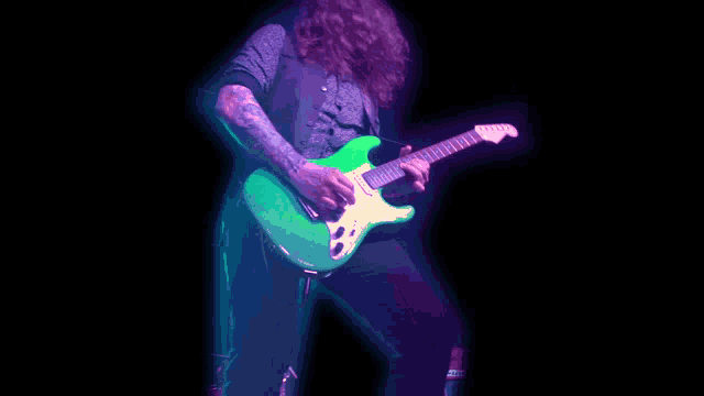 a man is playing a green guitar in the dark