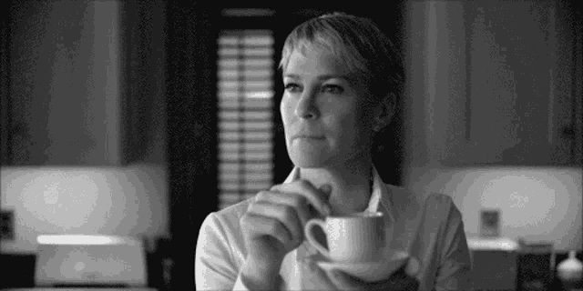 a woman in a white shirt is drinking a cup of coffee .