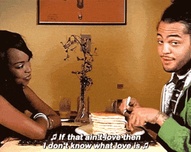 a man and a woman are sitting at a table with a stack of pancakes on a plate and the man is singing