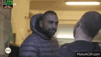 a man in a hooded jacket is talking to another man in a black shirt .