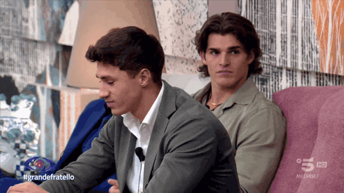 two men sitting on a couch with the hashtag grandefratello on the screen