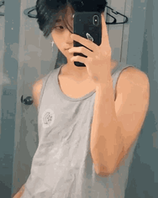 a young man in a tank top is taking a selfie with his cell phone .