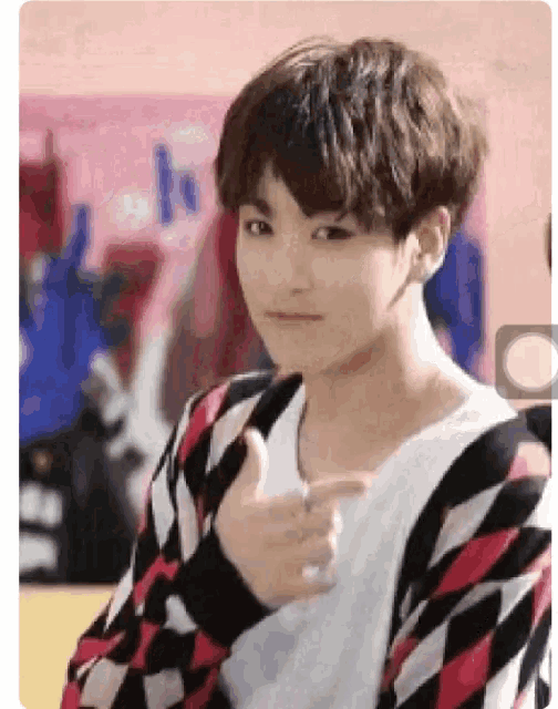 a young man is giving a thumbs up sign while wearing a checkered sweater .