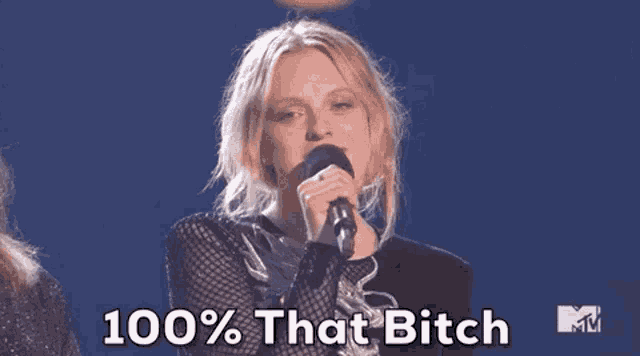 a woman singing into a microphone with the words 100 % that bitch behind her