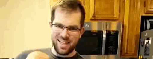 a man wearing glasses is holding a baby in his arms in a kitchen .