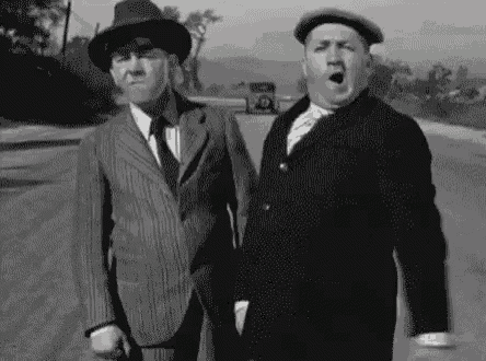 two men in suits and hats are walking down a road .