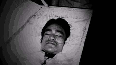 a black and white photo of a man in a coffin with his eyes closed .