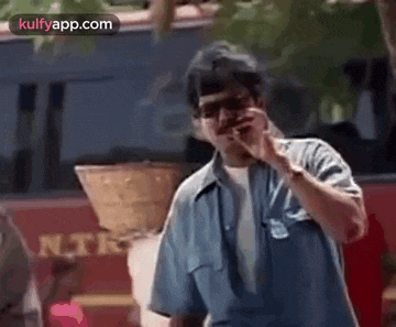 a man is talking on a cell phone in front of a red bus .