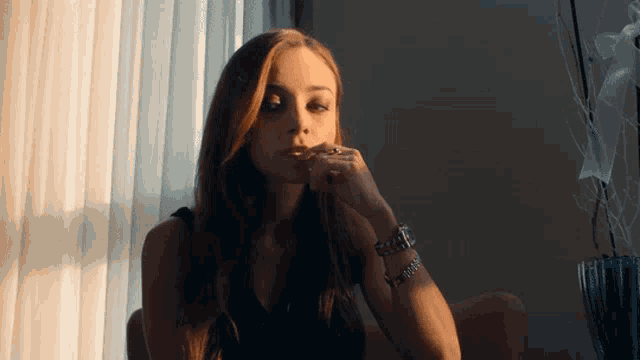 a woman sitting in front of a window with her hand on her face