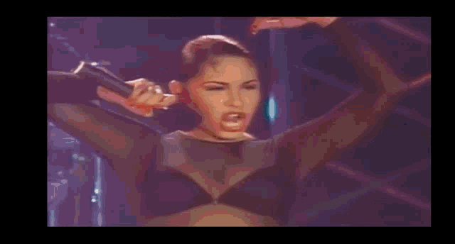 a woman is singing into a microphone with her arms in the air