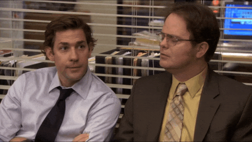 a man in a suit and tie sits next to another man in a shirt and tie