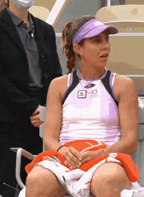 a woman wearing a purple visor is sitting in a chair with a tennis ball on her lap
