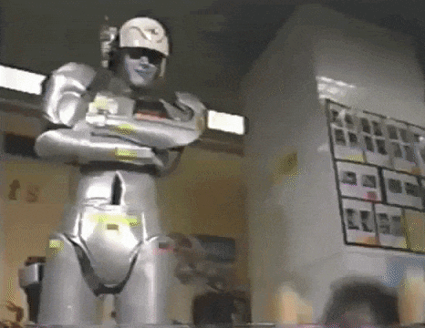 a robot is standing in a room with his arms crossed and a helmet on .