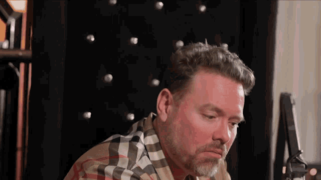 a man in a plaid shirt sits in a chair