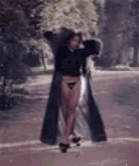 a woman in a long black coat is walking down a road .