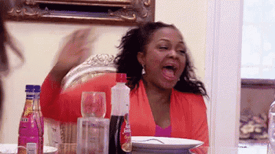 a woman is sitting at a table with her mouth open and a plate of food .