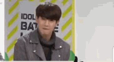 a man in a gray jacket is standing in front of a sign that says `` idol battle '' .