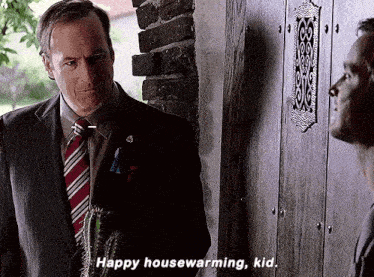a man in a suit and tie is talking to another man in front of a wooden door .