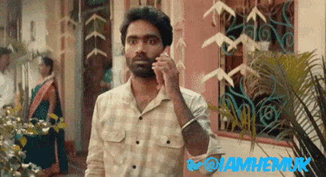 a man talking on a cell phone in front of a sign that says @iamhemuk