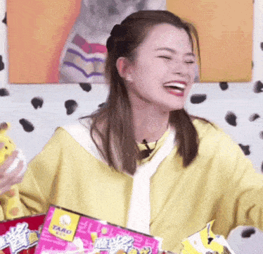 a woman in a yellow shirt is laughing while holding a bag of taro chips