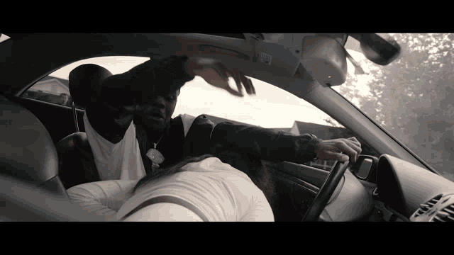 a man in a black jacket is driving a car with a woman in the back seat